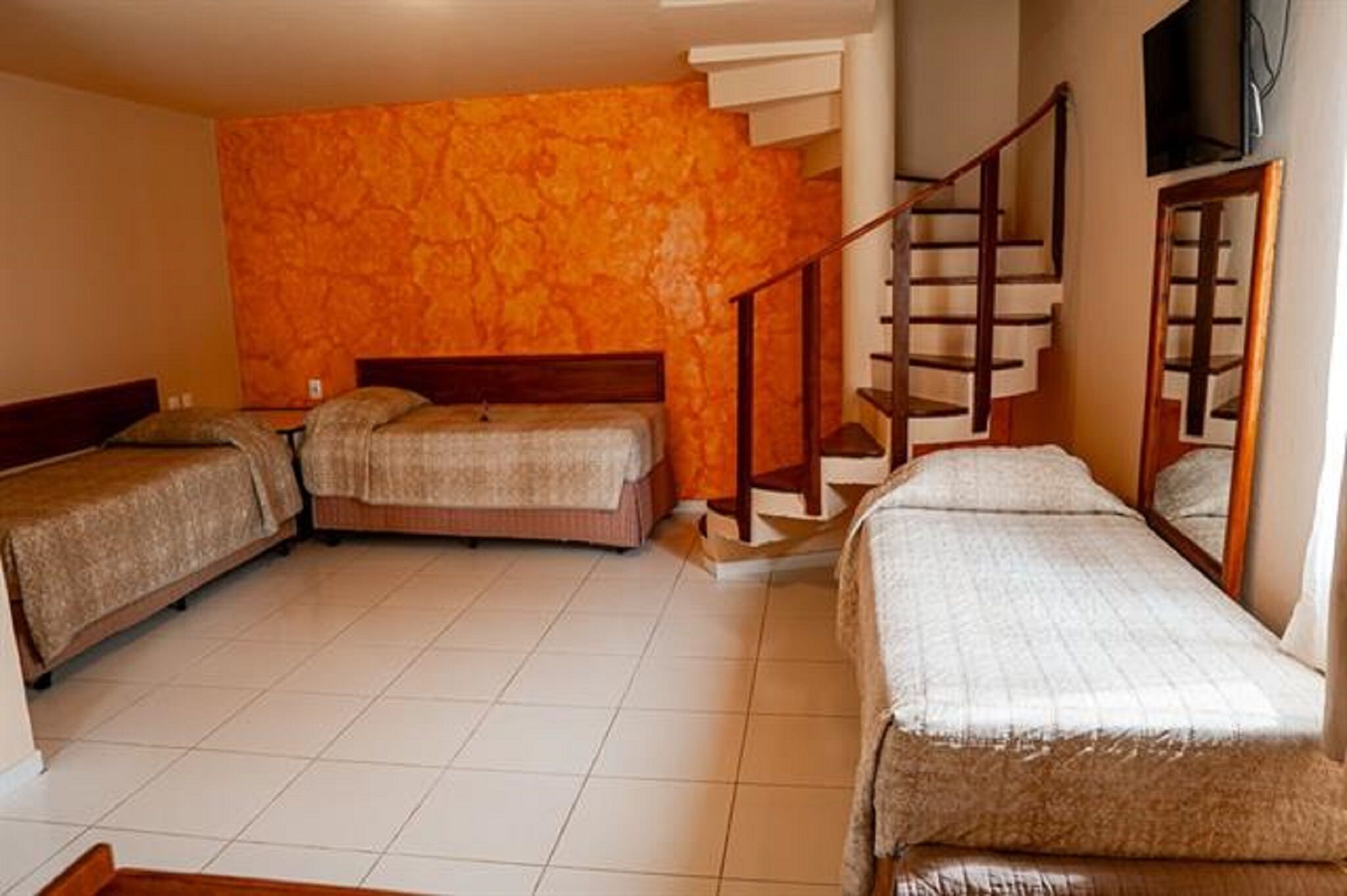 Une chambre avec trois lits, un escalier en bois et un téléviseur fixé au mur.