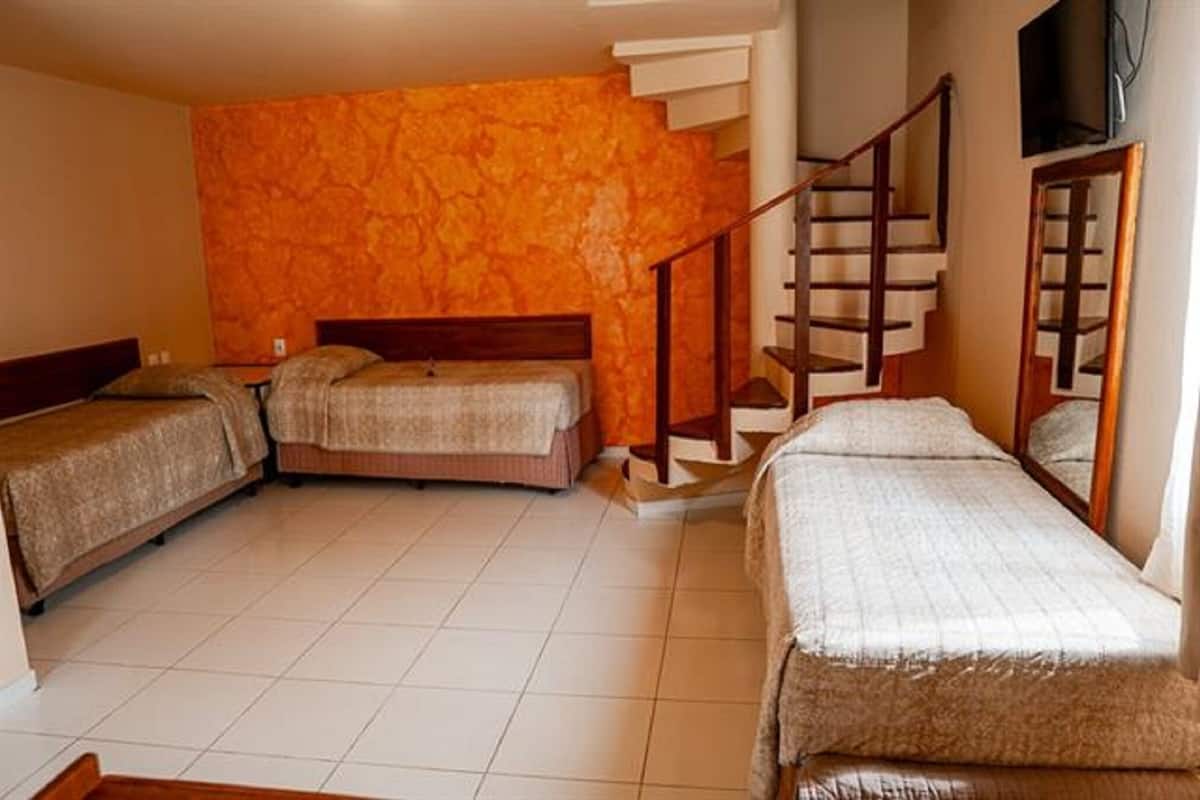 A room with three beds, a wooden staircase, and a TV mounted on the wall.