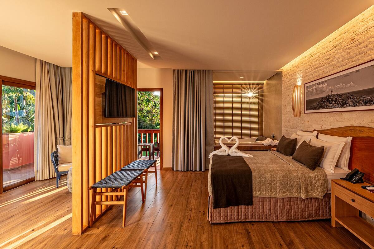 Een moderne hotelkamer met een groot bed, houten meubilair, een televisie en een balkon met gordijnen.