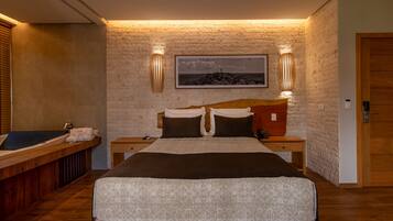 Quarto com uma cama grande, cabeceira de madeira, duas mesas de cabeceira, um quadro na parede e um banco de madeira com uma toalha.