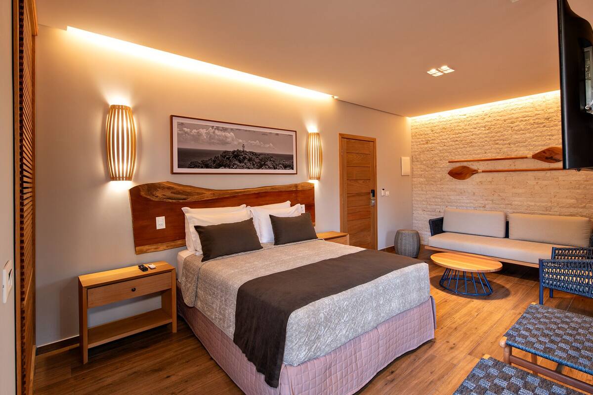 Een moderne slaapkamer met een groot bed, een houten hoofdbord, een aan de muur bevestigd schilderij en een accentmuur van steen.