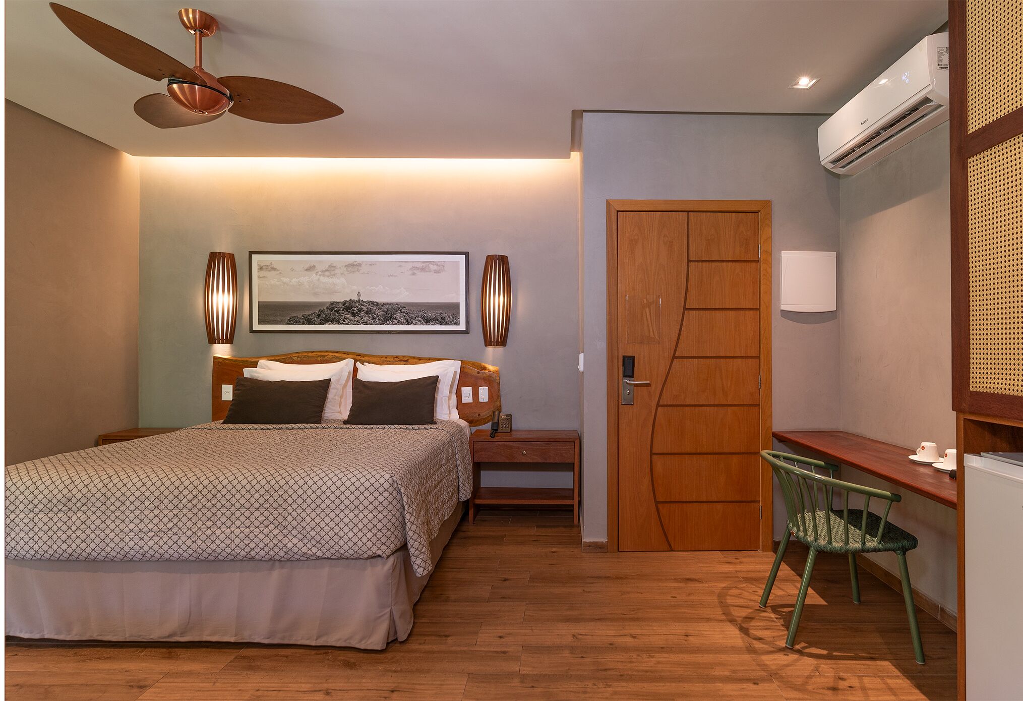 Quarto com cama, mesa de cabeceira, abajur e escrivaninha com cadeira.
