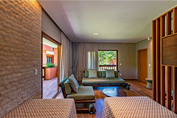 A room with a brick wall, a sofa set, a small table, and a view of an outdoor area with plants. - Village Paraíso Tropical (Cairu)