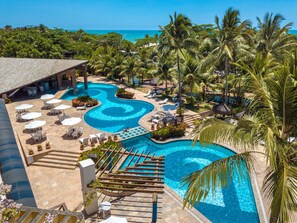 A resort with multiple swimming pools, lounge areas, and palm trees. - Portobello Praia (Porto Seguro)