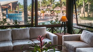 A poolside area with two cushioned seating arrangements, a potted plant, and a table with a lamp.