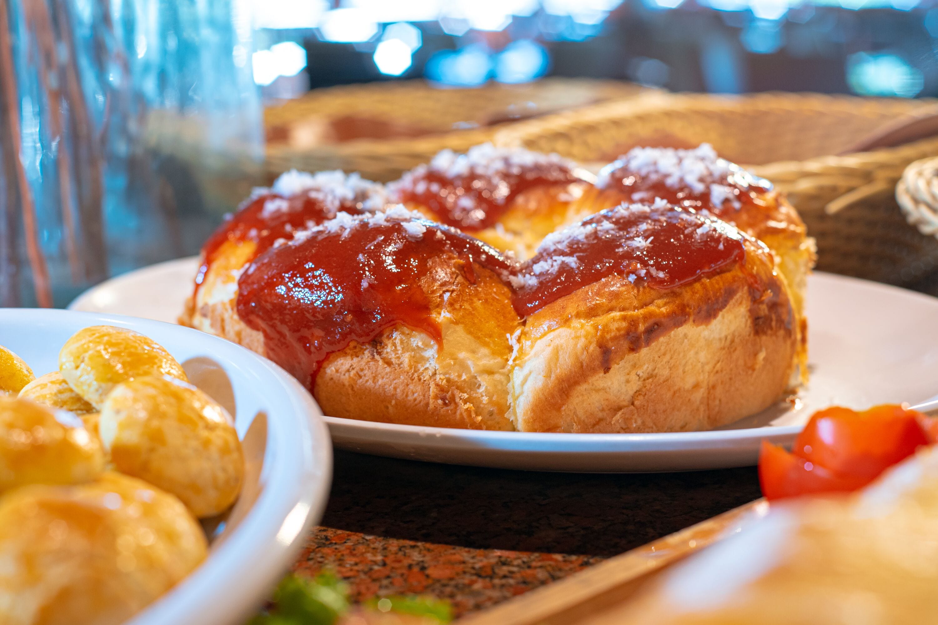 A plate of bread rolls with a glossy topping, possibly butter or jam, on a wooden table.