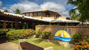 A hotel with a beach-themed sign, a covered patio, and lush landscaping.