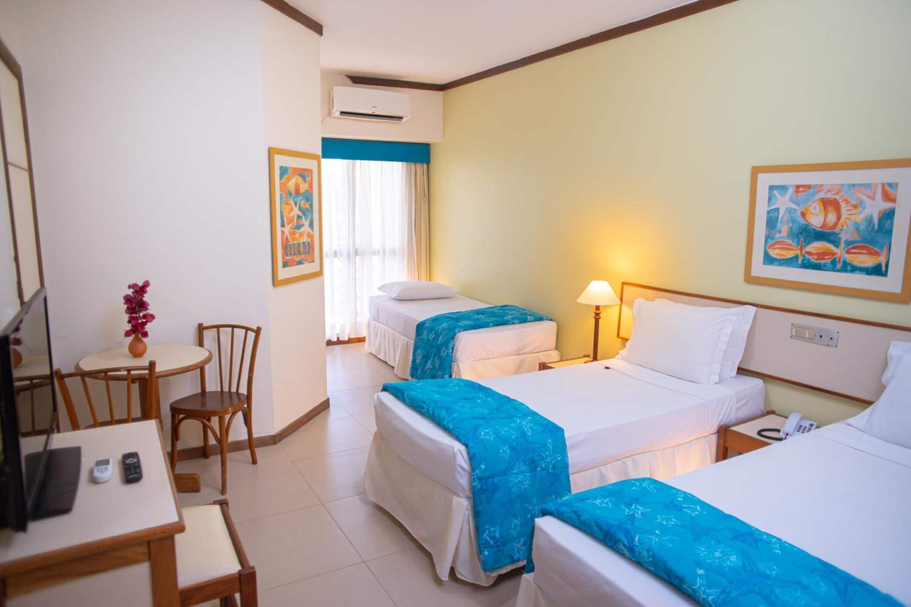 A hotel room with two beds, a desk, a chair, and a small table with a vase of flowers.
