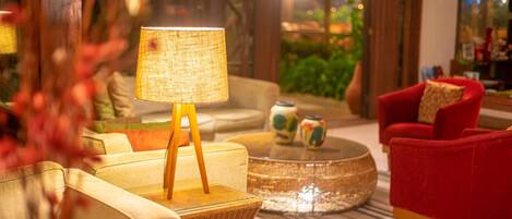 A cozy lobby with a wicker side table, a red armchair, and a lamp on a stand.