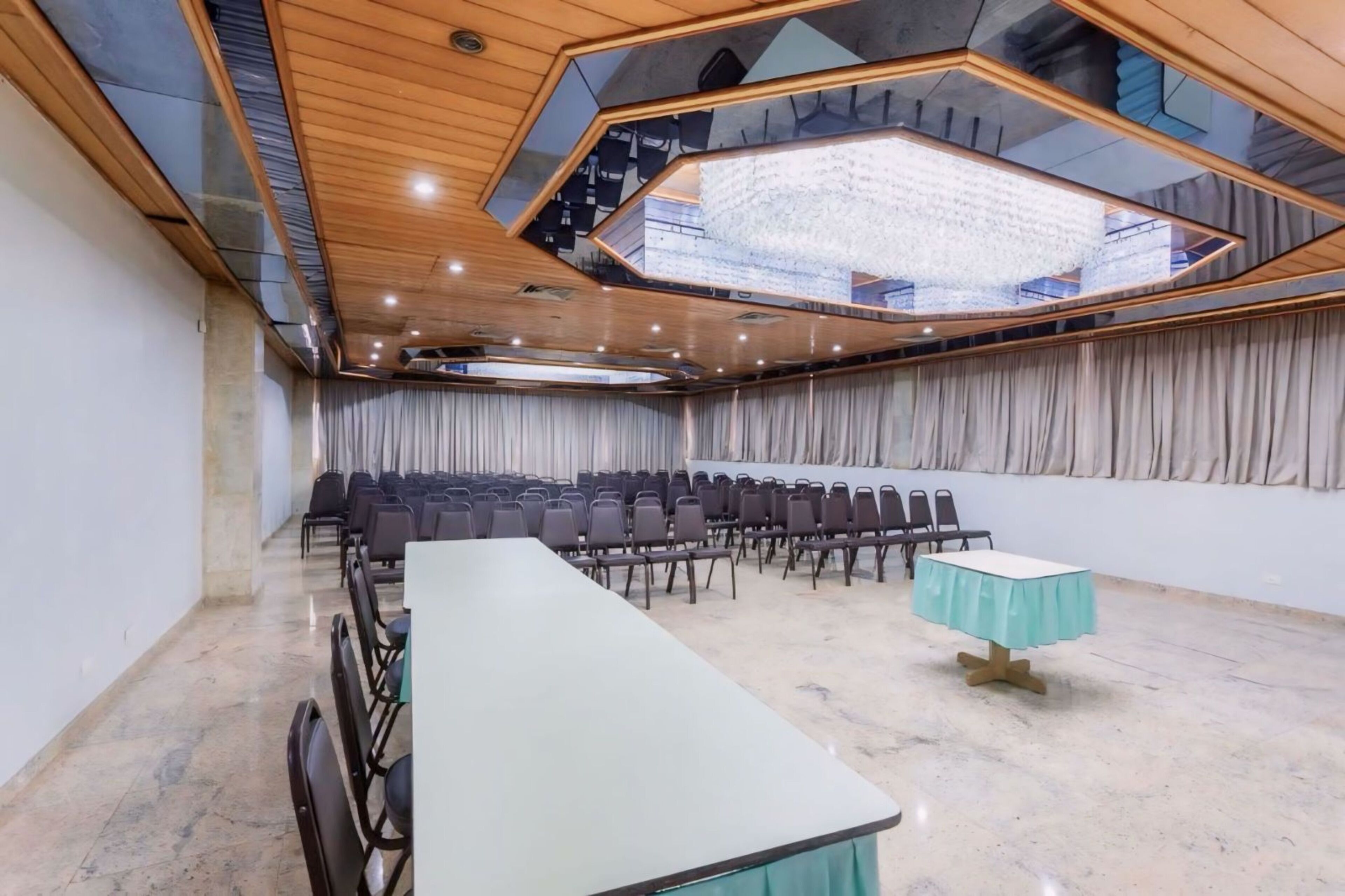 A conference room with a long table, rows of chairs, a chandelier, and a curtain backdrop.
