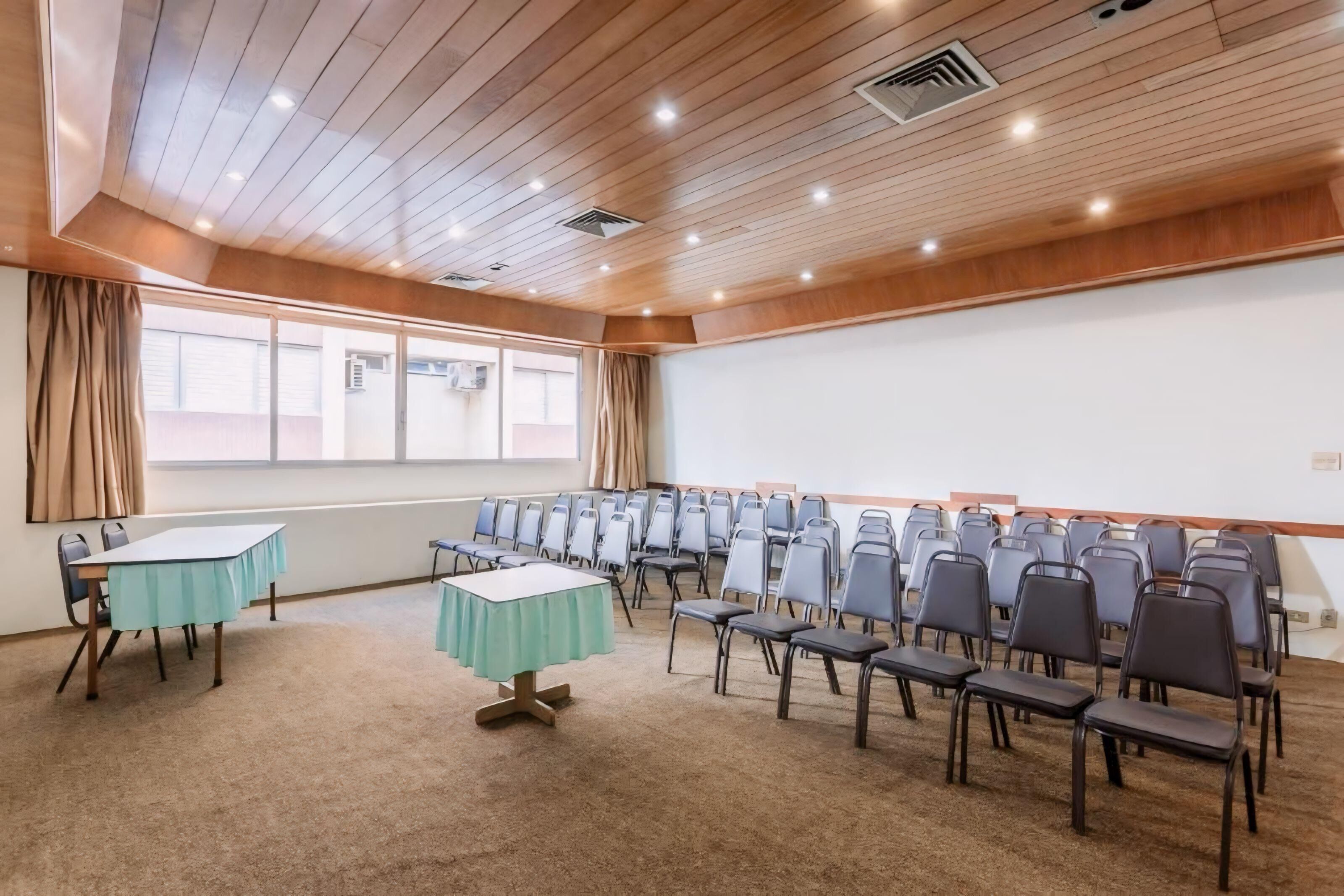 A conference room with wooden ceiling, carpeted floor, tables with green tablecloths, and rows of chairs.