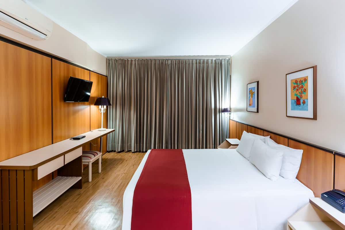 Ein Hotelzimmer mit Bett, Schreibtisch, Stuhl, Fernseher und einem Fenster mit Vorhängen.