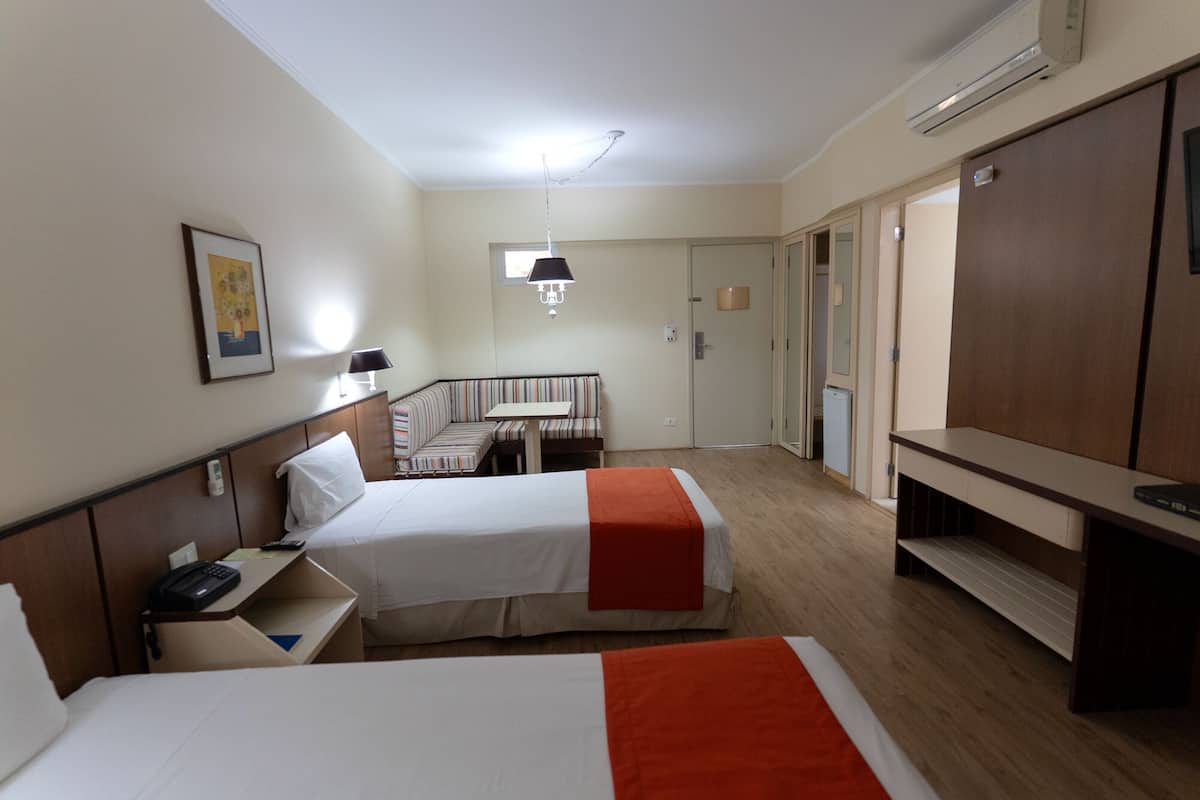 A hotel room with two beds, a desk, a chair, a TV, and a wardrobe.