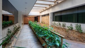 A modern hotel corridor with a skylight, stone walls, and a long planter with greenery. - Hotel Pan Americano (São Paulo)