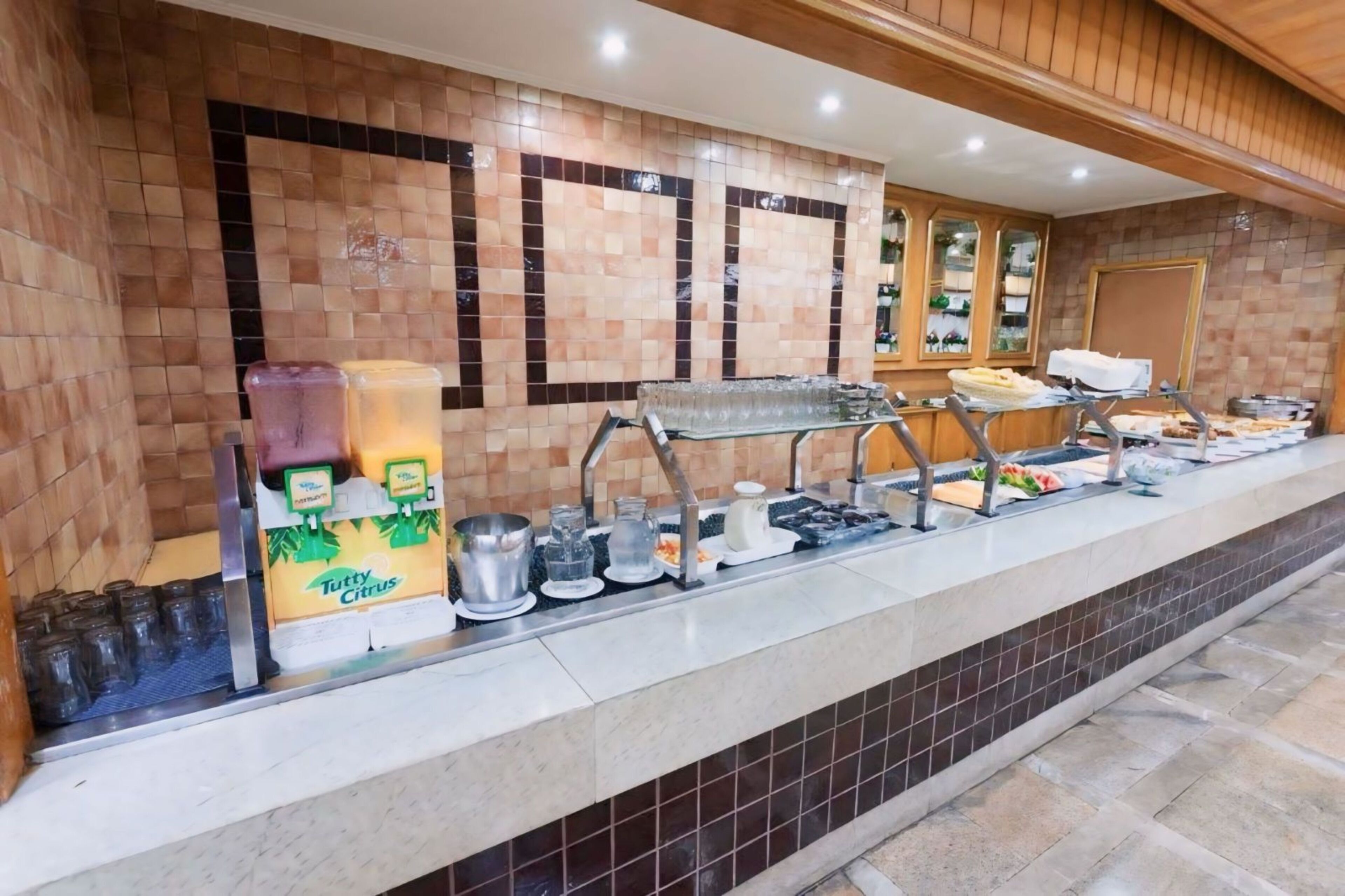 Un buffet proposant une variété de plats et de boissons, notamment un distributeur de jus d’orange TUTTY CITRUS, une machine à café et un assortiment de plats présentés sur un comptoir de service.