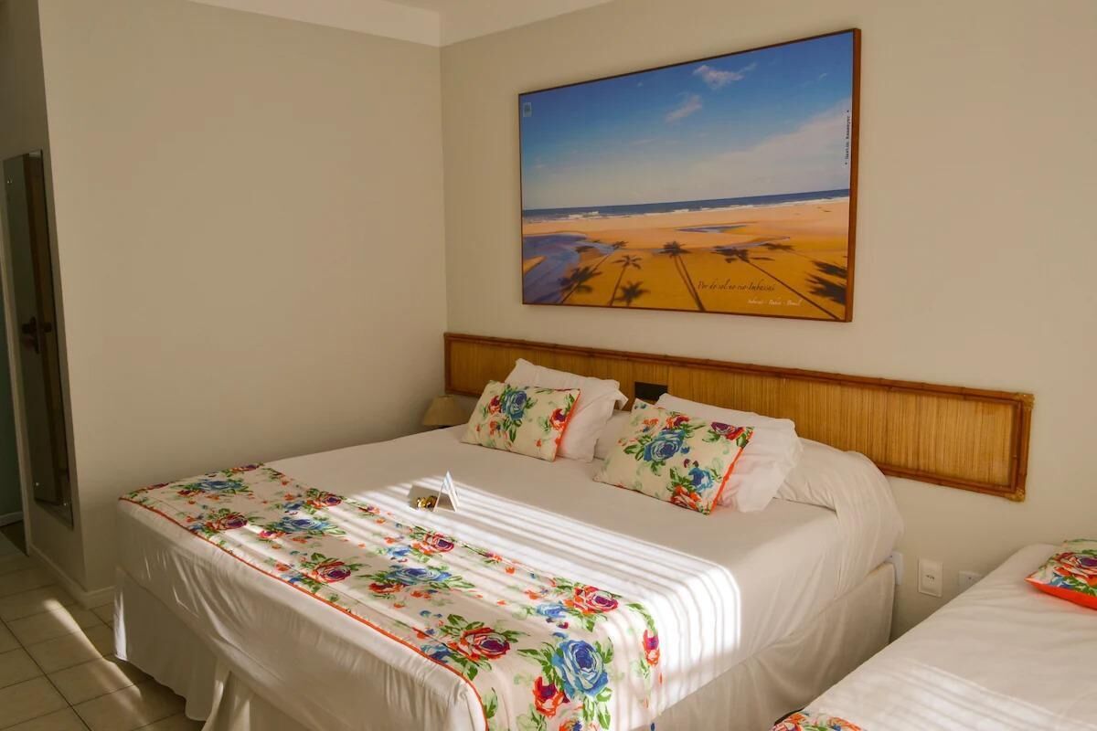 Una camera d'albergo con un letto, una testiera e un quadro raffigurante una spiaggia.