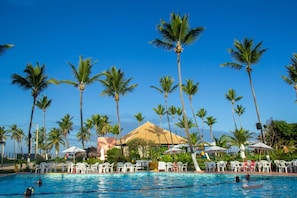 A pool area with palm trees, lounge chairs, and a thatched-roof building. - Hotel Resort Costa Dos Coqueiros (Mata de Sao Joao)
