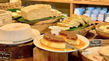 Una varietà di dolci esposti su supporti in legno, con etichette che indicano nomi come "Bau Ru" e "Adim de Tapioca".