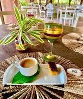 Uma mesa posta com uma xícara de café, um copo de bebida e uma sobremesa sobre uma folha.