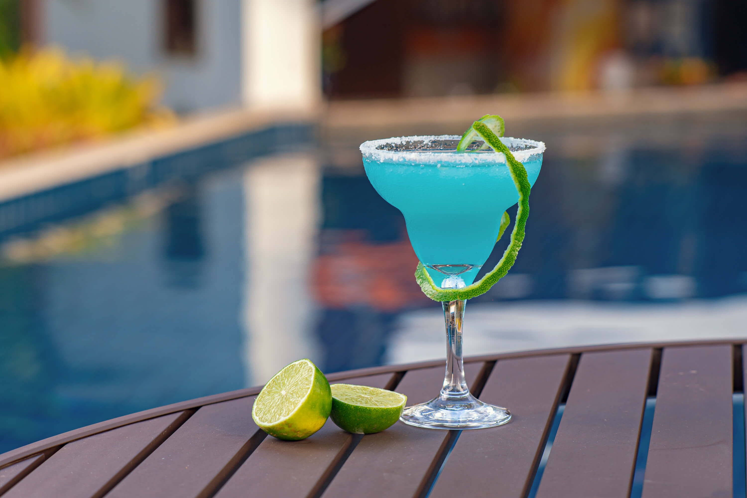 Ein Cocktail auf einem Tisch neben einem Pool, mit einer Limettenscheibe und einem Limettenstück.