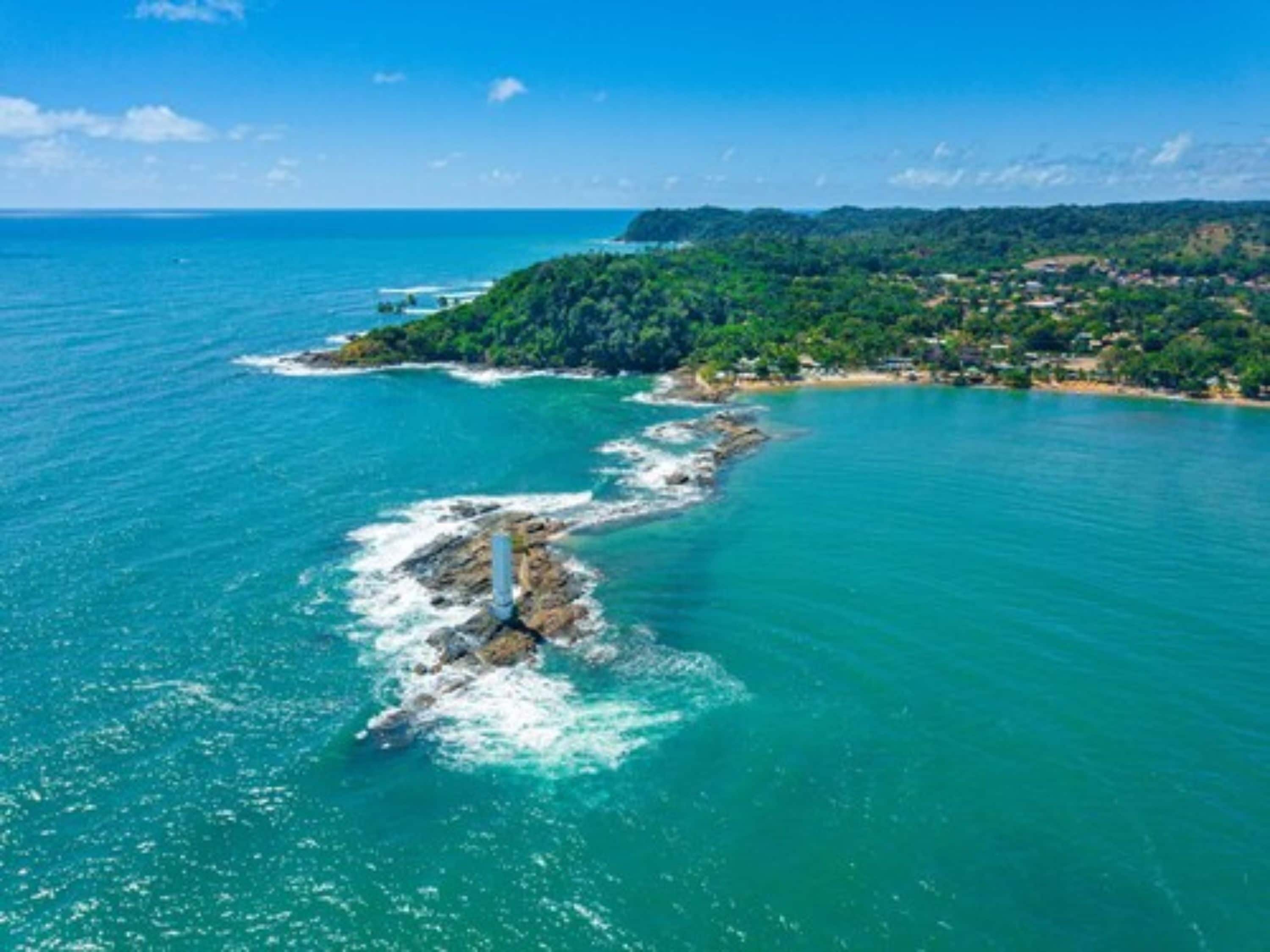 Vue aérienne d’une zone côtière avec un promontoire rocheux et une petite île couverte d’une végétation dense.