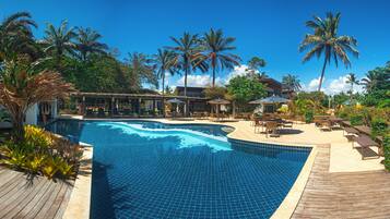 Piscina com deck de madeira, rodeada por palmeiras e espreguiçadeiras.