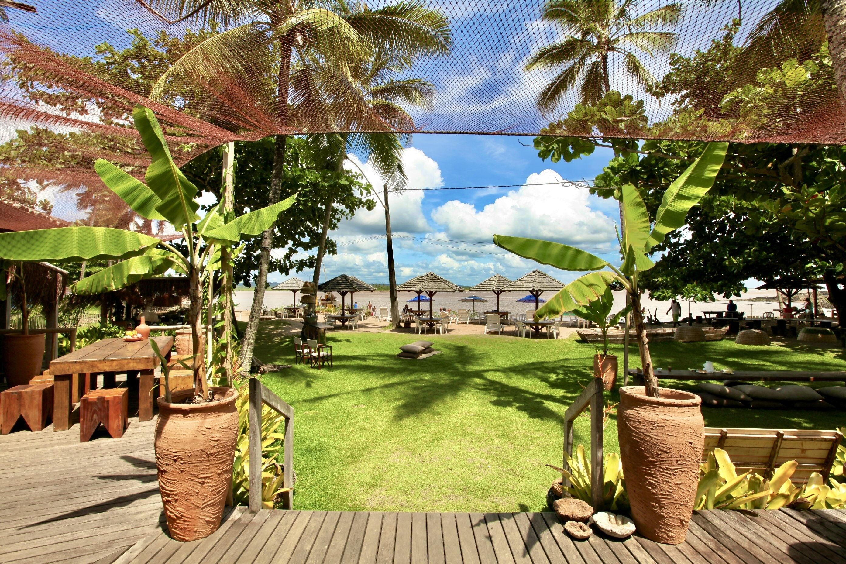A deck with a view of a pool area, surrounded by potted plants and outdoor furniture.