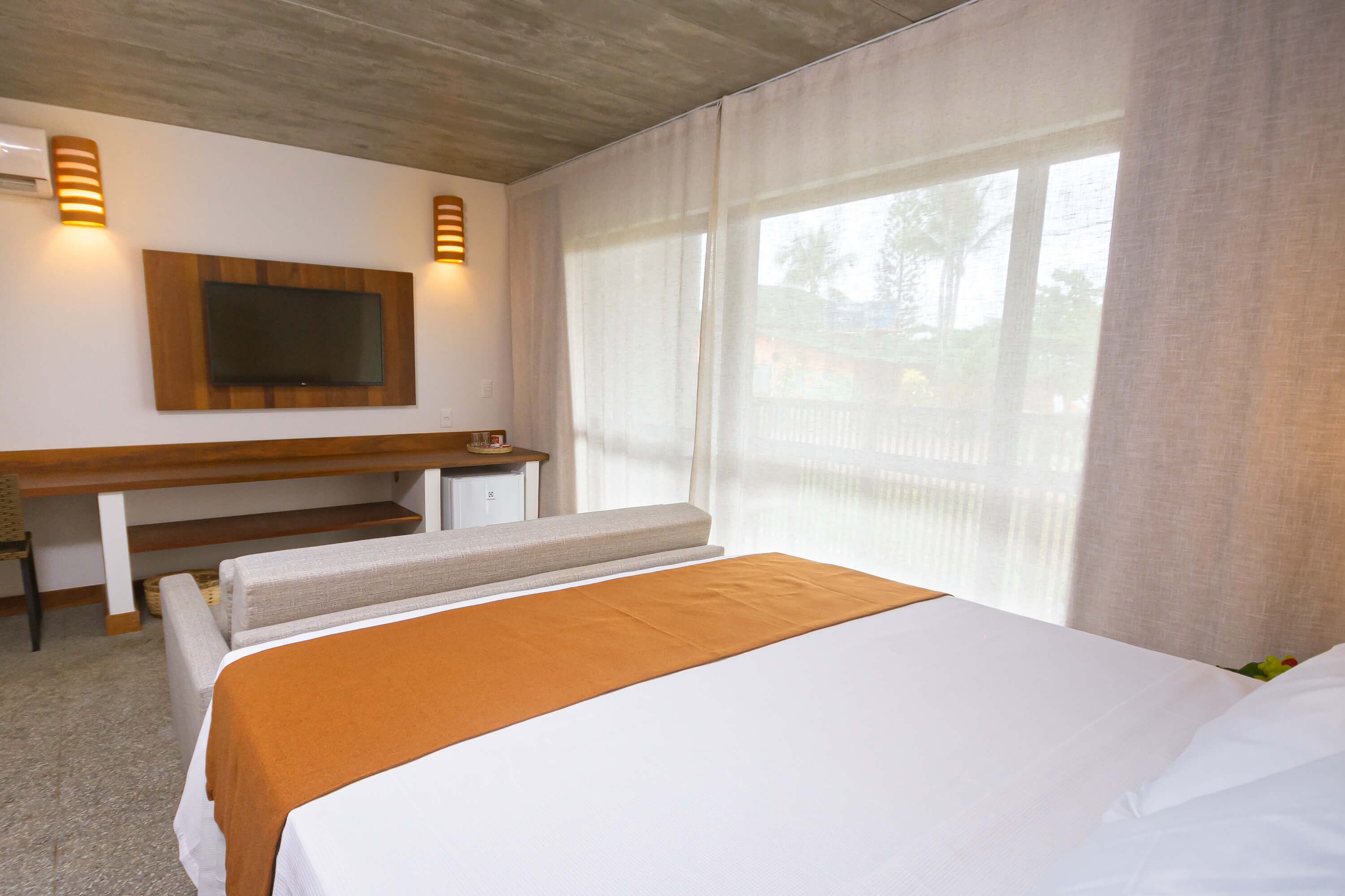Habitación de hotel con una cama grande, un escritorio, un televisor de pantalla plana y un ventanal con cortinas.