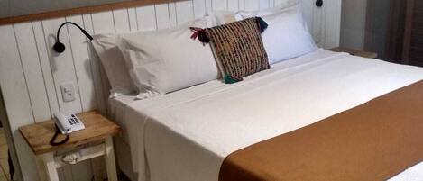 Un letto rifatto con lenzuola bianche e una coperta marrone, un comodino con un telefono, e un condizionatore d'aria a parete.