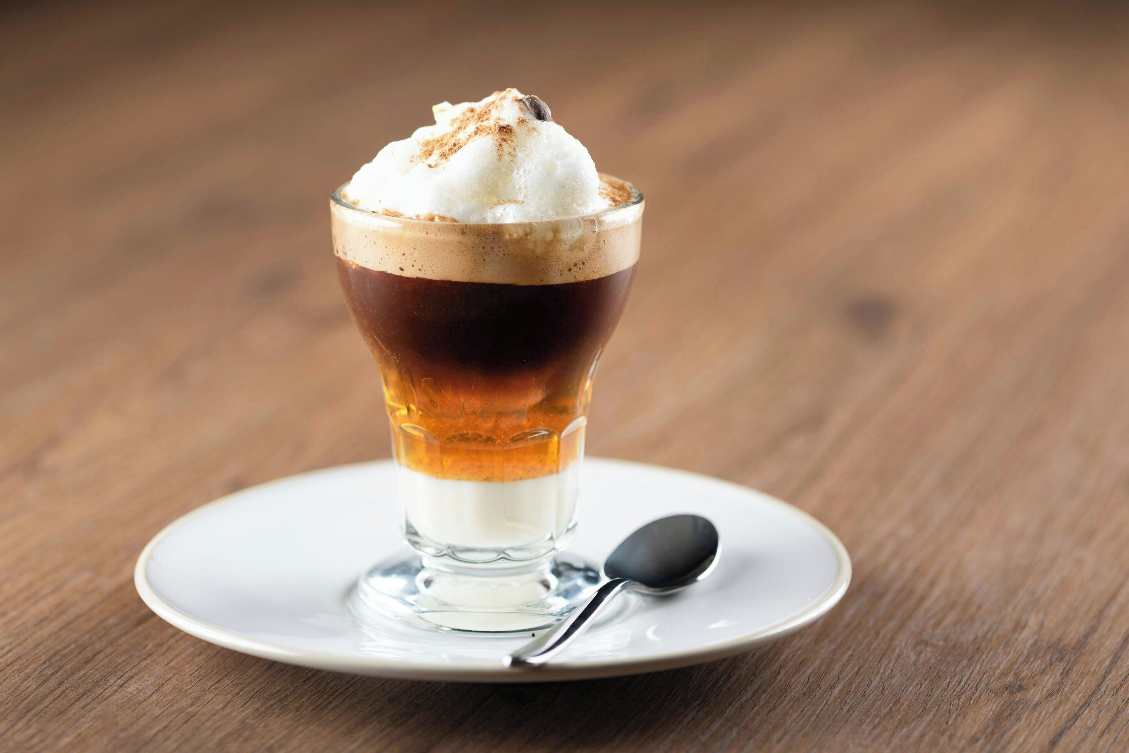 Un postre en un vaso sobre un plato blanco, con una cuchara a un lado.