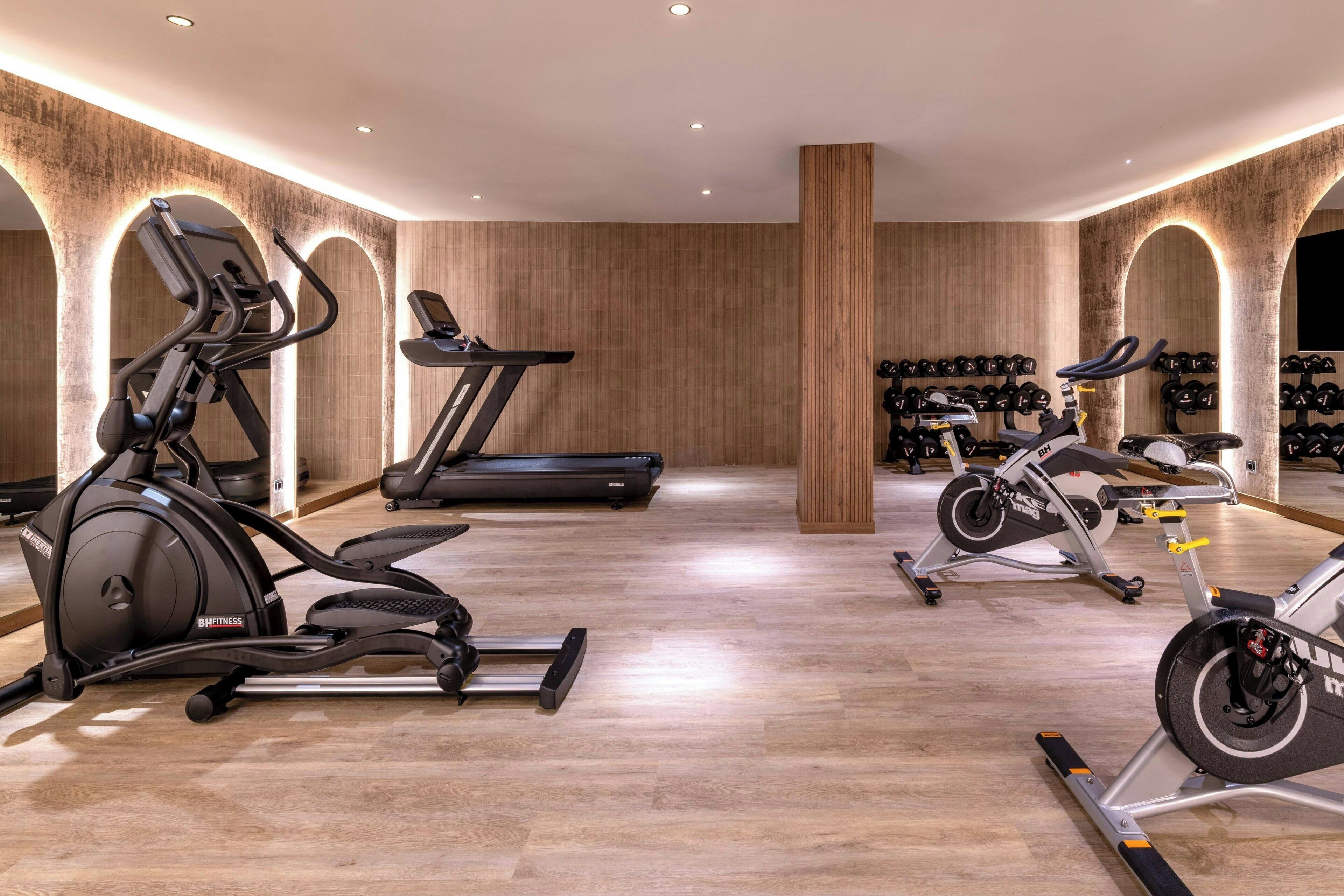 Un gimnasio con equipo cardiovascular, una cinta de correr y una pared de cascos.