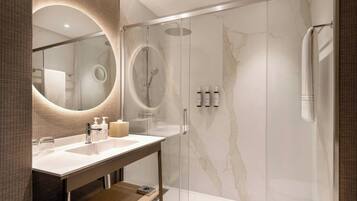 A modern bathroom with a glass-enclosed shower, a marble wall, and a vanity with a mirror and toiletries.