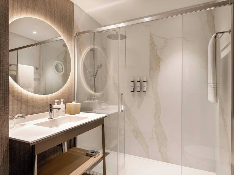 A modern bathroom with a glass-enclosed shower, a marble wall, and a vanity with a mirror and toiletries.