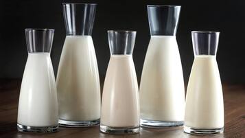 Cinco botellas de vidrio con leche sobre una superficie de madera.
