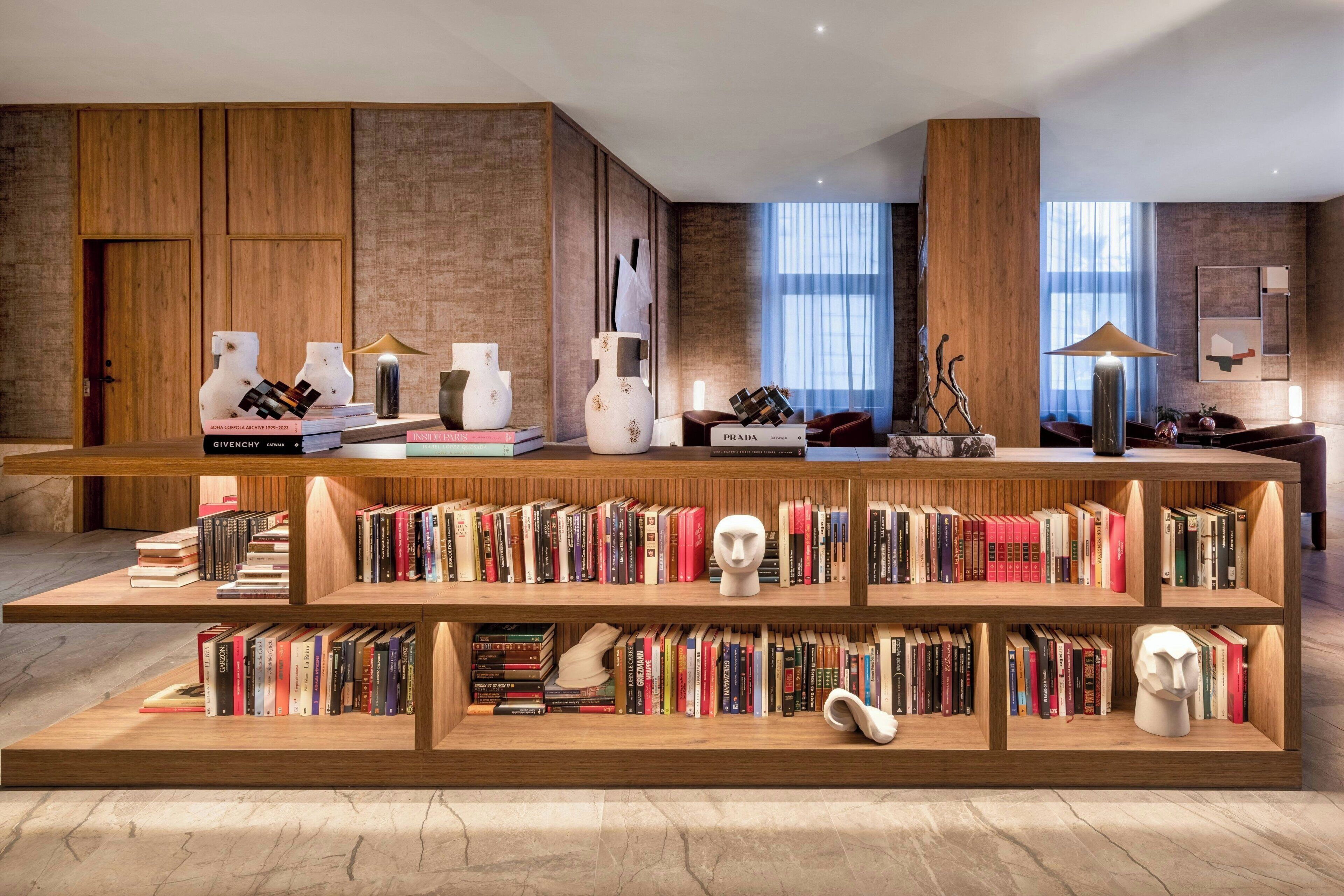 Una biblioteca moderna con estanterías de madera, suelo de mármol y un amplio ventanal con luz natural.