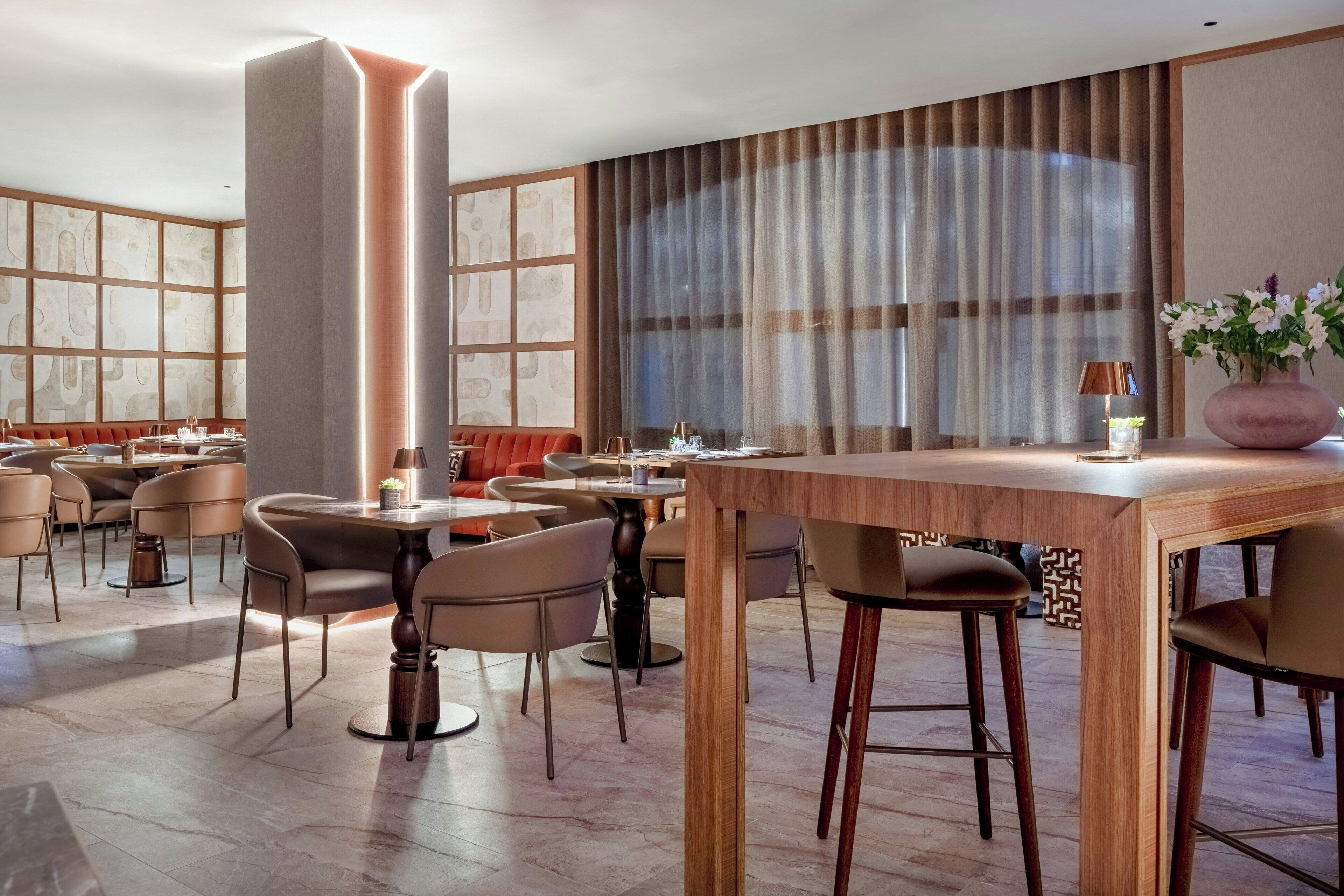 Un comedor moderno con mesas y sillas redondas, un pilar grande y vistas amplias a través de ventanas.