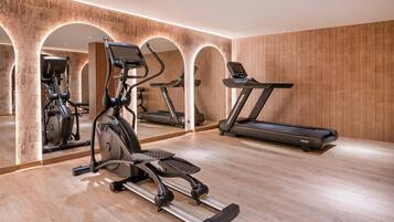 Une salle de sport équipée d’appareils de cardio, notamment des tapis de course et un appareil elliptique, dans une pièce aux murs en bois et dotée d’un mur miroir.