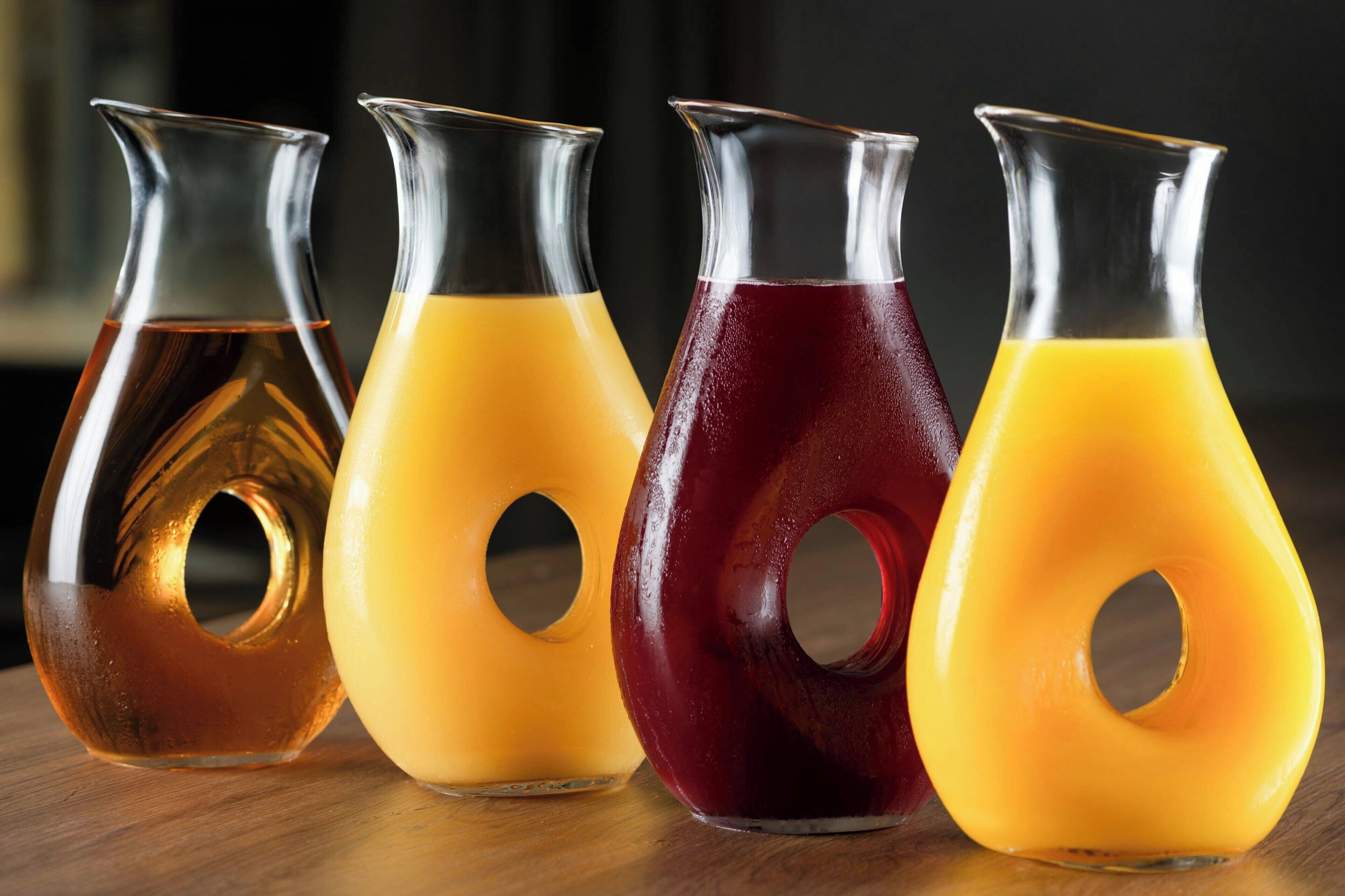Vier Glasflaschen mit bunten Flüssigkeiten auf einer Holztischplatte.