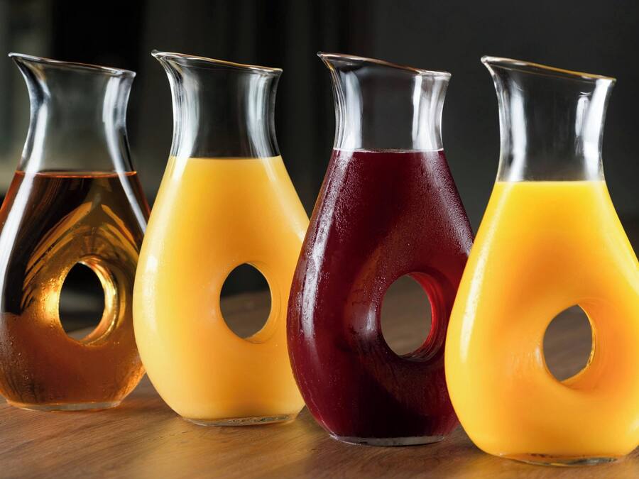 Vier Glasflaschen mit bunten Flüssigkeiten auf einer Holztischplatte.