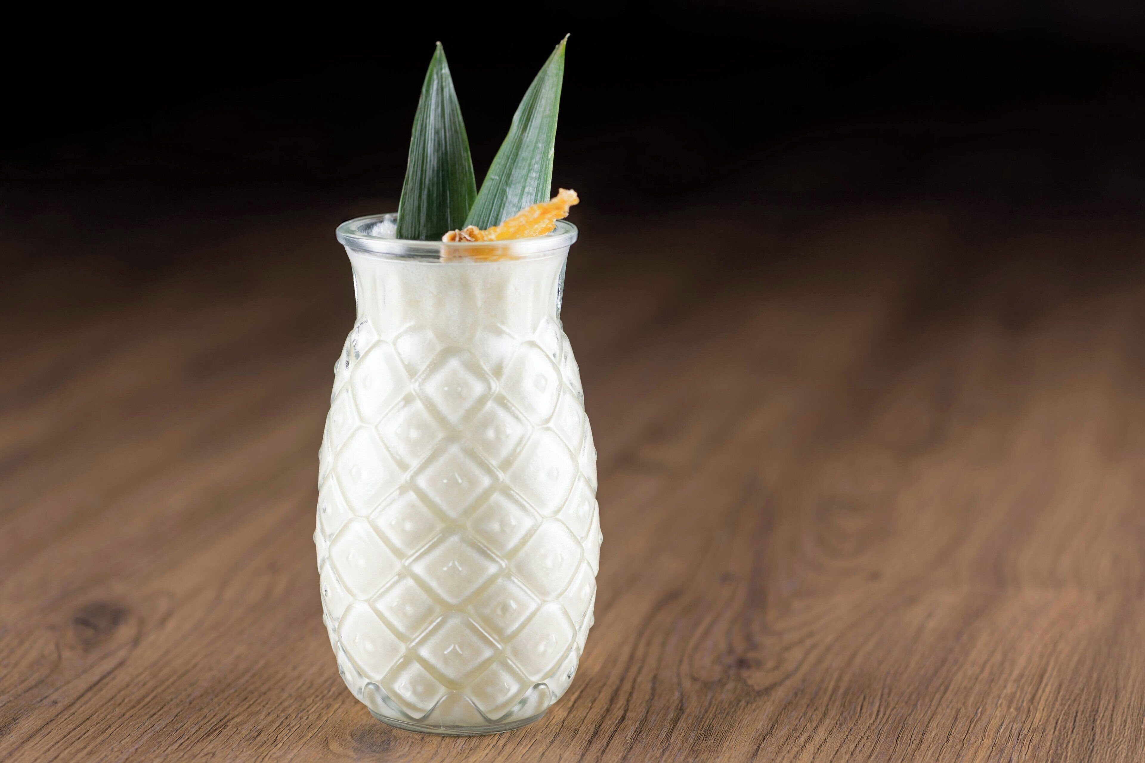 Un vas de vidre texturat amb una planta de pineapple sobre una superfície de fusta.