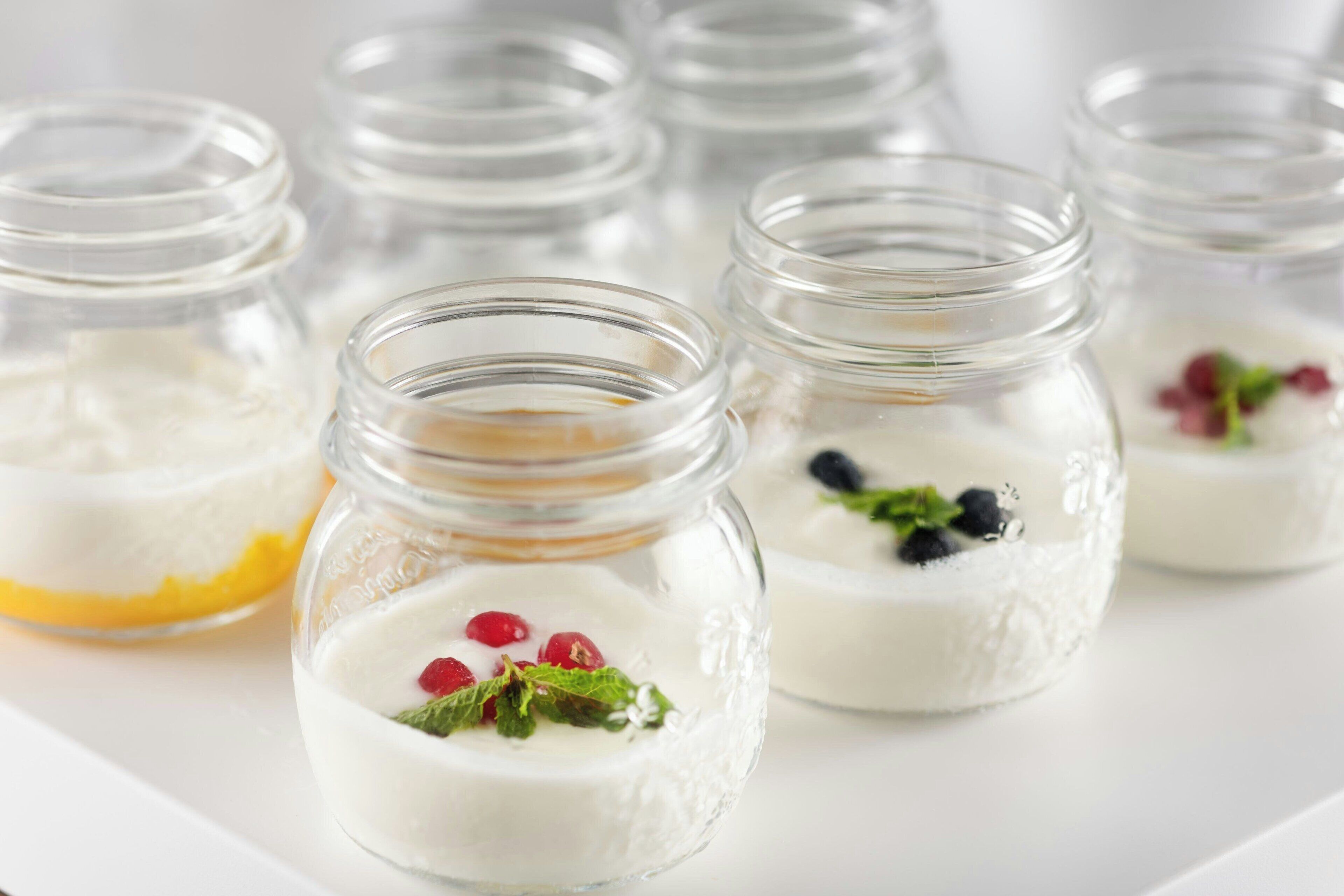Several glass jars containing a creamy dessert with berries and mint leaves.