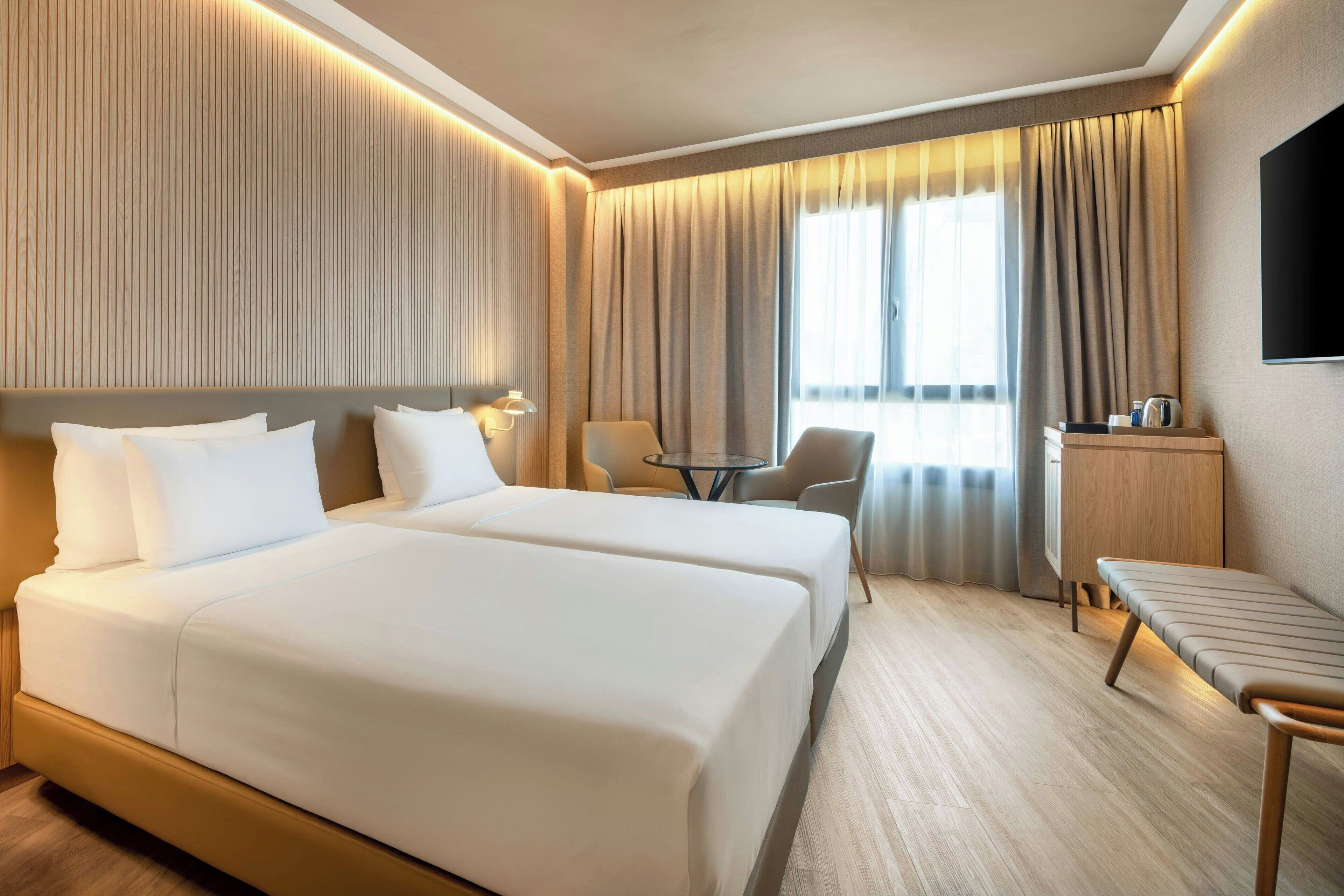 Habitación de hotel con dos camas, un escritorio, una silla, un televisor y una ventana con cortinas.