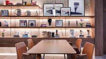Un interior moderno con una mesa y sillas de madera, estanterías con libros y objetos decorativos, y una pared de mármol.
