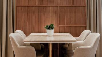 A dining area with a square table, four beige upholstered chairs, and a potted plant on the table.