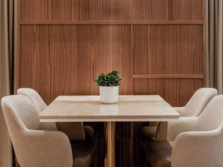 A dining area with a square table, four beige upholstered chairs, and a potted plant on the table.