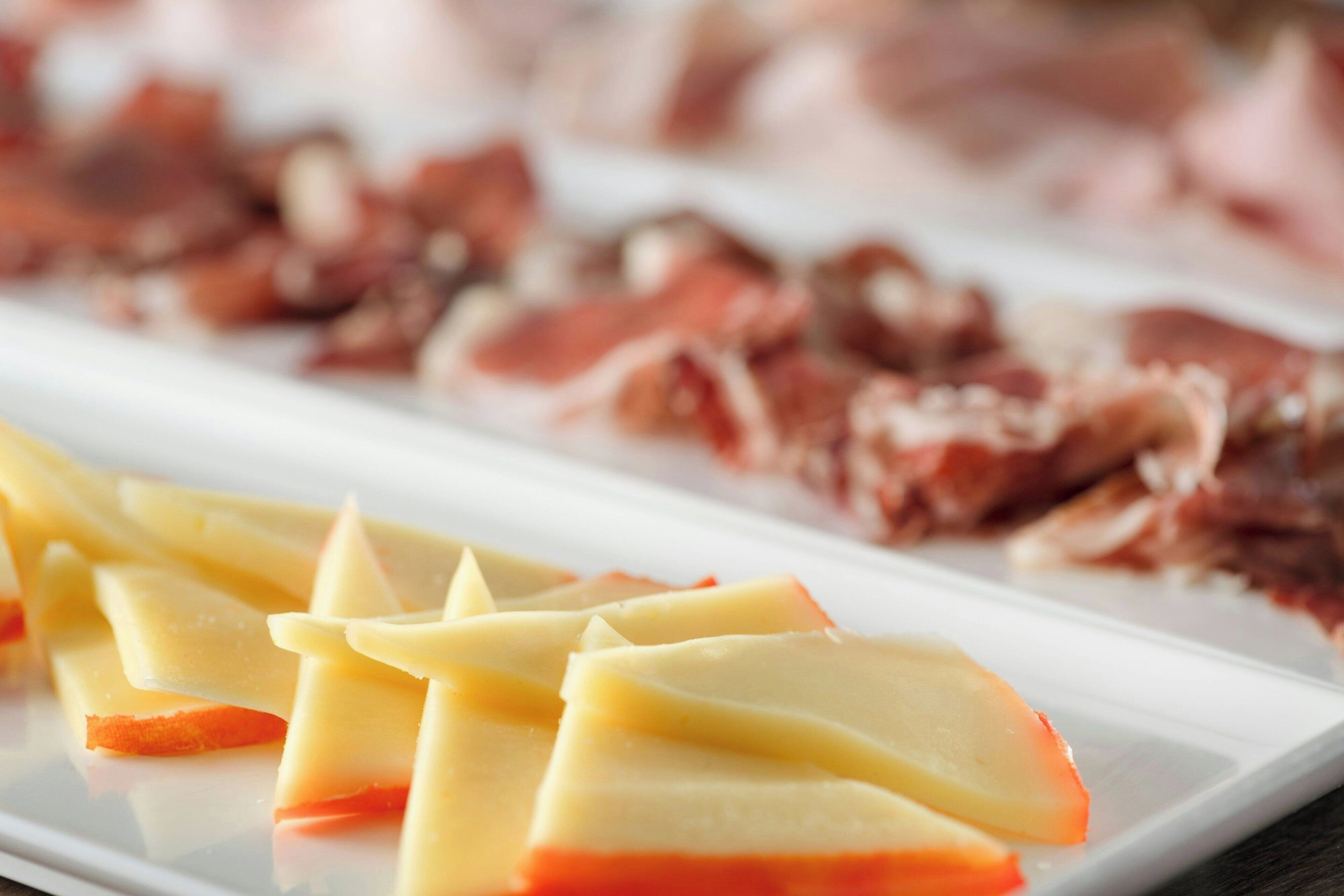 Um prato retangular branco com fatias de queijo e embutidos dispostas de forma organizada.