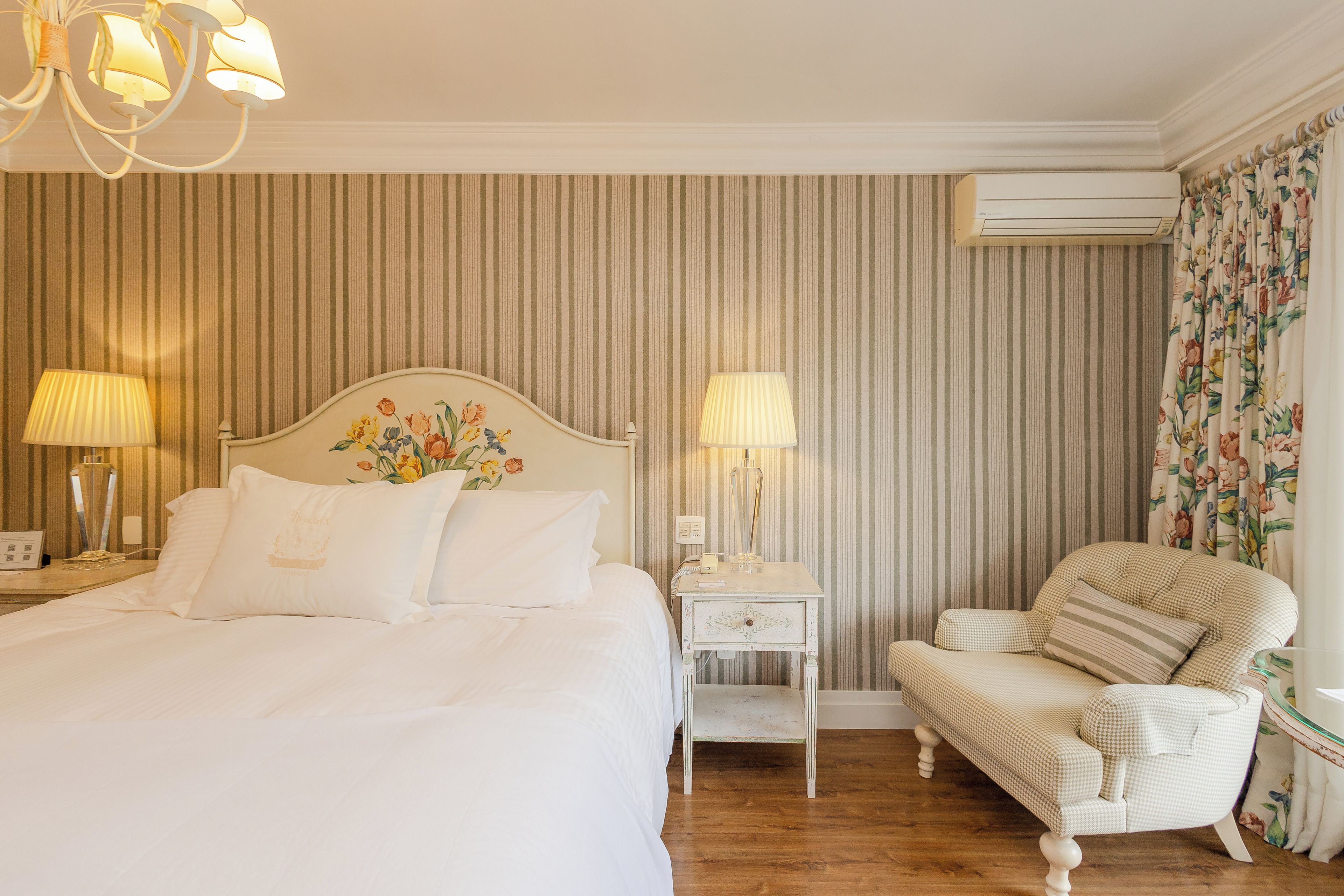 Habitación de hotel con cama, lámparas de noche, mesita, una silla y equipo de aire acondicionado.