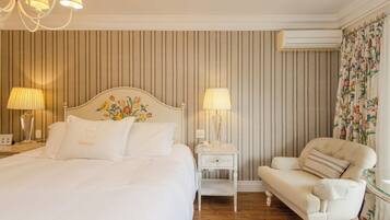Habitación de hotel con cama, lámparas de noche, mesita, una silla y equipo de aire acondicionado.