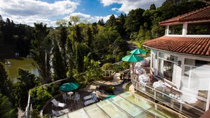 A hotel with a terrace overlooking a lake, surrounded by lush greenery. - Estalagem St Hubertus (Gramado)
