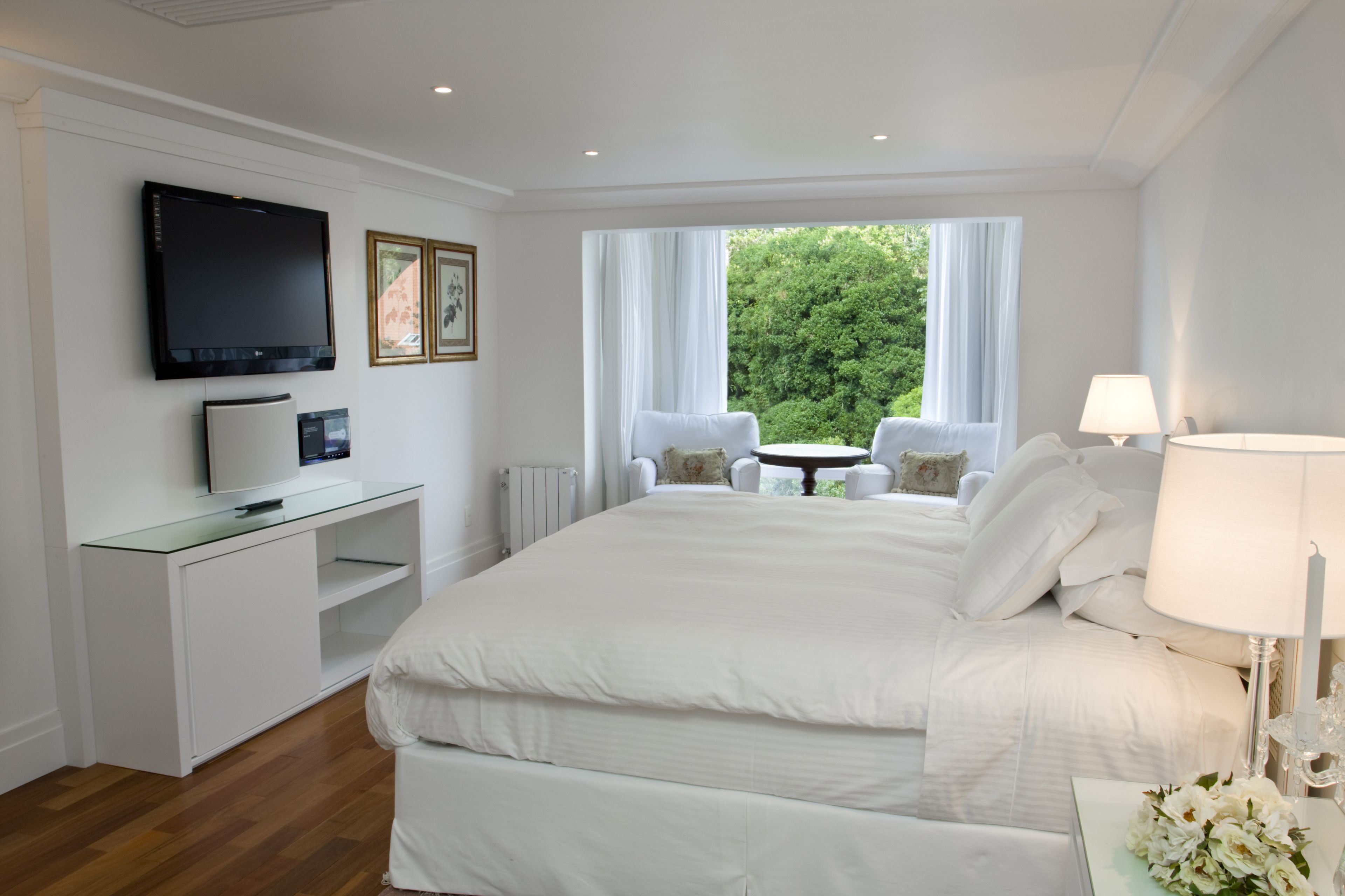 Une chambre d’hôtel avec un grand lit, une télévision, une petite table avec des chaises et une vue sur la verdure.